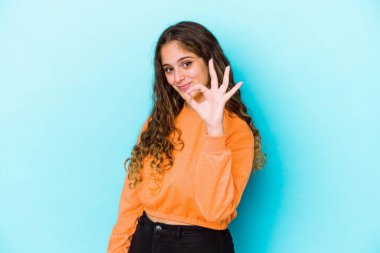 Kafkasyalı kıvırcık saçlı genç kadın göz kırpıyor ve elleriyle iyi bir jest yapıyor..