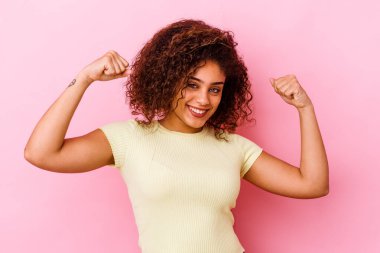 Pembe arka planda izole edilmiş genç Afrikalı Amerikalı kadın güçlü bir hareket sergiliyor, kadın gücünün sembolü.