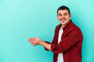 Mavi arka planda izole edilmiş genç beyaz bir adam palmiyesinde bir kopya alanı tutuyor..