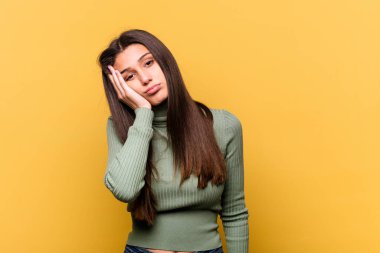 Sarı arka planda izole edilmiş genç Hintli kadın yorgun ve uykulu ellerini başının üstünde tutuyor..