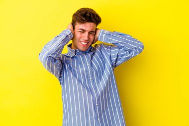 Sarı arka planda izole edilmiş genç beyaz adam elleriyle kulakları örtüyor..