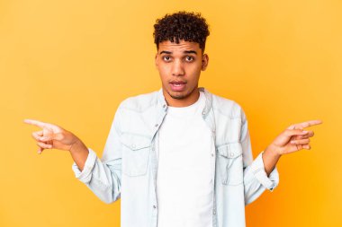 Genç Afro-Amerikalı kıvırcık adam, mor üzerine izole edilmiş, farklı fotokopi alanlarına bakıyor, birini seçiyor, parmaklarıyla gösteriyor..