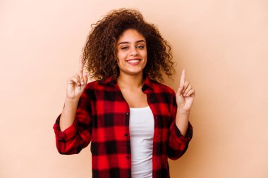 Bej arka planda izole edilmiş genç Afrikalı Amerikalı kadın iki parmağı da boş bir alan gösteriyor..