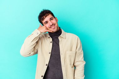 Mavi arka planda izole edilmiş genç beyaz adam parmaklarıyla bir cep telefonu hareketi gösteriyor..