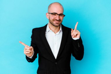 Genç, beyaz, kel bir adam mavi arka planda izole edilmiş farklı fotokopi alanlarını gösteriyor, birini seçiyor, parmaklarıyla gösteriyor..