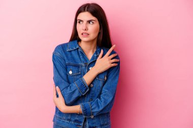 Pembe arka planda izole edilmiş genç beyaz kadın kafası karışmış, kuşkulu ve güvensiz hissediyor..