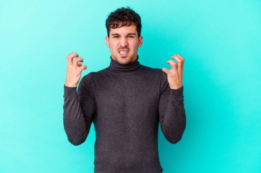 Mavi arka planda izole edilmiş genç beyaz adam gergin elleriyle çığlık atıyor..