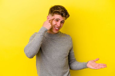 Sarı arka planda izole edilmiş genç beyaz adam işaret parmağıyla hayal kırıklığı jesti yapıyor..