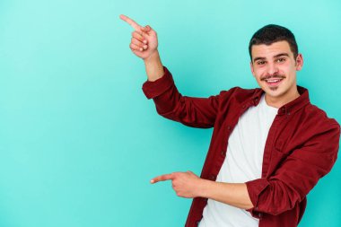 Kafkasyalı genç adam mavi arka planda izole edilmiş. İşaret parmağıyla işaret ettiği için heyecanlı..