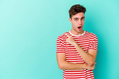 Mavi arka planda izole edilmiş genç beyaz adam yan tarafı işaret ediyor.