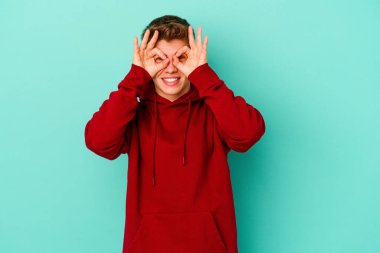 Mavi arka planda izole edilmiş genç beyaz adam gözlerinde sorun olmadığını gösteriyor.