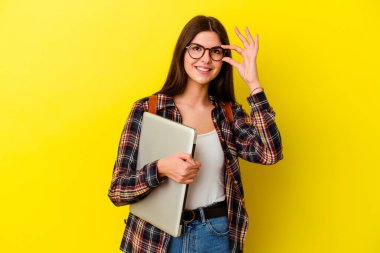 Pembe arka planda dizüstü bilgisayar tutan beyaz bir kadın heyecanlı..