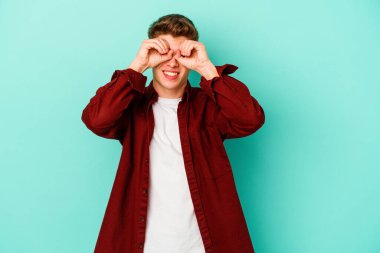 Mavi arka planda izole edilmiş genç beyaz adam gözlerinde sorun olmadığını gösteriyor.