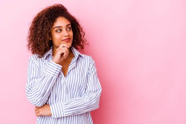 Genç Afrikalı Amerikalı kadın pembe arka planda izole edilmiş şüpheli ve şüpheci bir ifadeyle yana bakıyor..