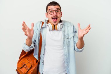 Beyaz arka planda müzik dinleyen beyaz tenli genç bir öğrenci zaferi ya da başarıyı kutluyor, şaşırıyor ve şok oluyor..