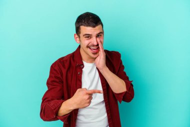 Kafkasyalı genç adam mavi arka planda izole edilmiş. Dedikodu yapıyor, bir şeyleri bildiriyor..
