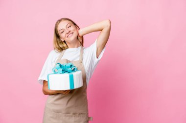 Genç Rus fırıncı kadın lezzetli bir pasta tutuyor kafasının arkasına dokunuyor, düşünüyor ve bir seçim yapıyor..