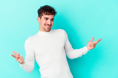 Kafkasyalı genç adam mavi arka planda izole edilmiş neşeli bir şekilde gülüyor. Mutluluk kavramı.