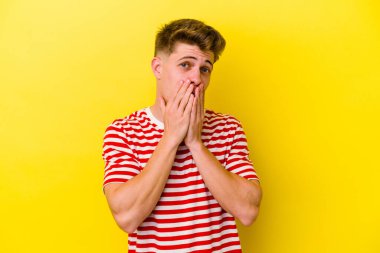 Sarı arka planda izole edilmiş genç beyaz adam şok olmuş, ağzı ellerle kaplanmış, yeni bir şey keşfetmeye hevesli..