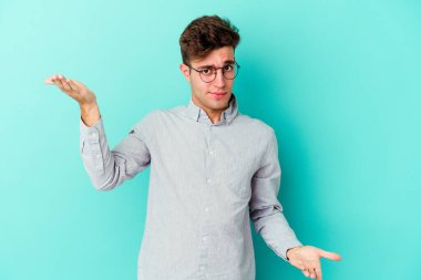 Mavi arka planda izole genç beyaz adam kollarıyla ölçek yapar, mutlu ve kendinden emin hisseder..