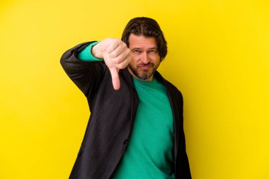 Sarı arka planda izole edilmiş orta yaşlı beyaz adam baş parmağını aşağı gösteriyor, hayal kırıklığı konsepti..