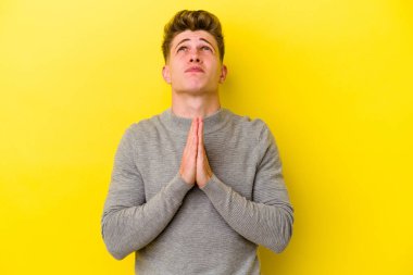 Sarı arka planda izole edilmiş genç beyaz bir adam el ele tutuşup ağız kenarında dua ediyor, kendinden emin hissediyor..
