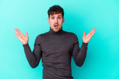 Kafkasyalı genç adam mavi arka planda izole edildi. Şaşırdı ve şok oldu..