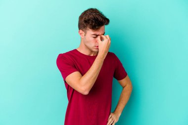 Kafkasyalı genç bir adam mavi arka planda izole edilmiş, başı ağrıyor, yüzüne dokunuyor..