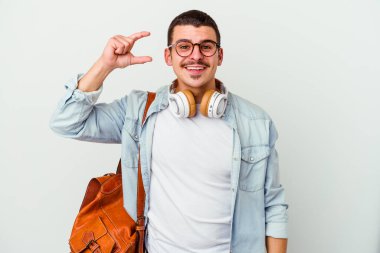 Beyaz arka planda izole edilmiş müzik dinleyen beyaz tenli genç bir öğrenci işaret parmaklarıyla küçük bir şey tutuyor, gülümsüyor ve kendinden emin..
