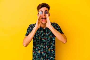 Sarı arka planda izole edilmiş Hawaii tişörtü giyen genç beyaz bir adam heyecanlı bir şekilde öne doğru bağırıyor..