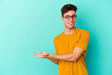 Mavi arka planda izole edilmiş genç beyaz bir adam palmiyesinde bir kopya alanı tutuyor..