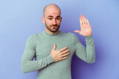 Kafkasyalı genç kel adam mor arka planda izole edilmiş yemin ediyor, elini göğsüne koyuyor..