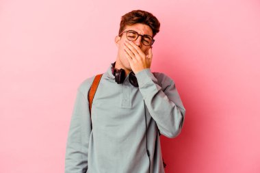 Pembe arka planda izole edilmiş genç bir öğrenci esniyor. Ağzıyla ağzını kapatan yorgun bir hareket sergiliyor..