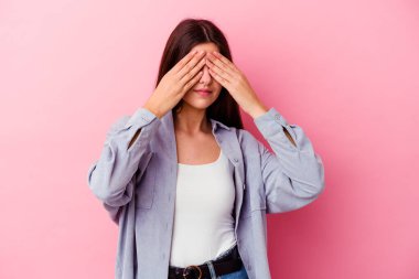 Pembe arka planda izole edilmiş genç beyaz kadın elleriyle gözlerini kapatmaktan korkuyor..