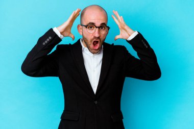 Genç, beyaz, kel bir adam mavi arka planda bir zaferi ya da başarıyı kutlarken şaşırmış ve şok olmuştu..