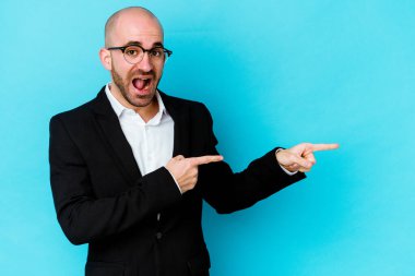 Genç beyaz tenli kel adam mavi arka planda izole edildi. İşaret parmaklarıyla işaret ederek heyecanlandı..