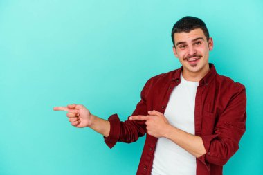 Mavi arka planda izole edilmiş genç beyaz adam işaret parmağıyla fotokopi alanını işaret ederek heyecan ve arzusunu ifade ediyor..