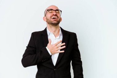 Genç, beyaz, kel bir adam mavi arka planda izole edilmiş. Yüksek sesle gülüyor, elini göğsüne koyuyor..