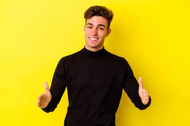 Sarı arka planda izole edilmiş genç beyaz adam iki eliyle bir şey tutuyor, ürün sunumu..