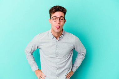 Kafkasyalı genç adam mavi arka planda izole edilmiş komik ve dost canlısı bir dil uzatıyor..