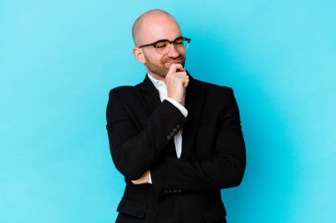 Genç, beyaz, kel bir adam mavi arka planda izole edilmiş düşünüyor ve yukarı bakıyor, yansıtıyor, düşünüyor, hayal kuruyor..