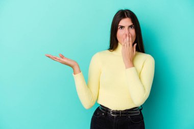 Mavi arka planda izole edilmiş genç beyaz kadın, avuç içinin fotokopi alanını tutmaktan etkilenmiş..