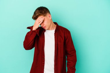 Genç beyaz adam mavi arka planda izole edilmiş tapınaklara dokunuyor ve başı ağrıyor..