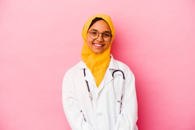 Genç doktor Müslüman kadın pembe arka planda izole edilmiş mutlu, güler yüzlü ve neşeli..