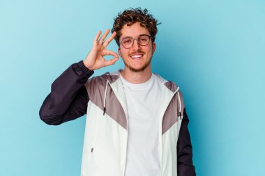 Gözlüklü genç beyaz adam mavi arka planda izole edilmiş neşeli ve kendinden emin..