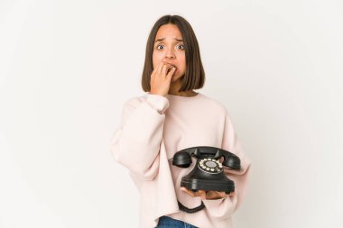 Antika bir telefon tutan genç İspanyol kadın tırnak yiyor, gergin ve çok endişeli..