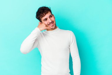 Mavi arka planda izole edilmiş genç beyaz adam parmaklarıyla bir cep telefonu hareketi gösteriyor..