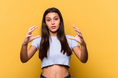 Sarı arka planda izole edilmiş genç bir Hintli kadın elinde avuç içi bir şeyle kameraya sunuyor..