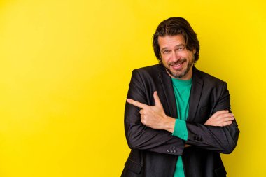 Sarı arka planda izole edilmiş orta yaşlı beyaz adam işaret parmağıyla işaret ederek gülümsüyor..