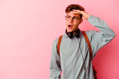 Pembe arka planda izole edilmiş genç bir öğrenci. Uzağa bakıyor. Elini alnına koyuyor..